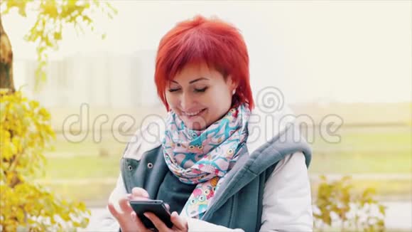 秋天漂亮的女人有着白种人的眼睛有着炽热的头发在街上兴高采烈地使用手机视频的预览图