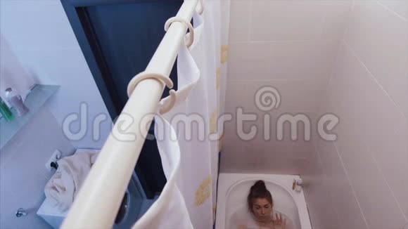 浴室里有耳机的漂亮女人在泡泡浴里听音乐的女人视频的预览图
