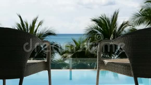 全高清在靠近海滩的游泳池前放大两张放松的度假椅椰子棕榈树和海景视频的预览图