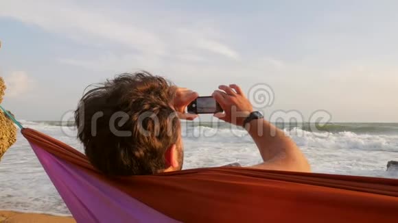 一个年轻人在海边的吊床上休息用手机给大海拍照高清慢行克里米亚俄罗斯视频的预览图