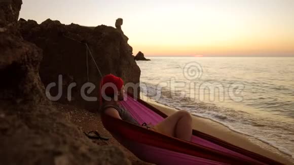 年轻的白种人躺在沙滩上的吊床上欣赏着令人惊叹的金色日落美景1920x1080视频的预览图