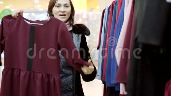 一个穿着毛皮大衣的女人在服装店里挑选一件衣服视频的预览图