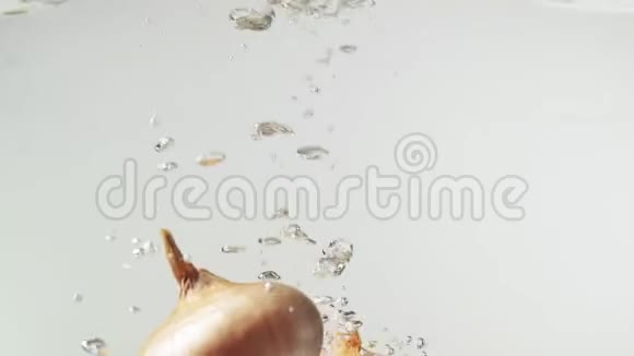 慢动作黄色洋葱落入水中白色背景视频的预览图