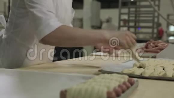 在面包店里一位面包师女士擀面团用生泡芙糕点包裹香肠生的热狗卷起来视频的预览图