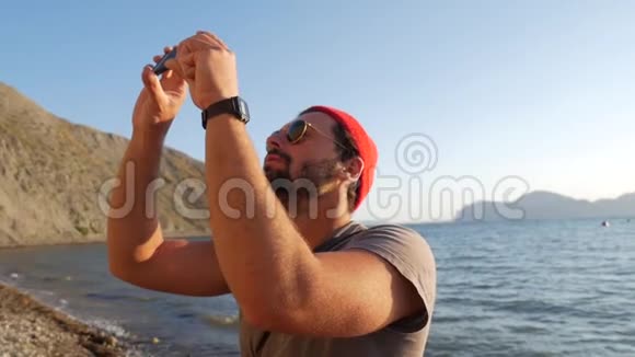 年轻潮人白种人在海滩上用手机拍摄视频高清慢镜头克里米亚俄罗斯视频的预览图