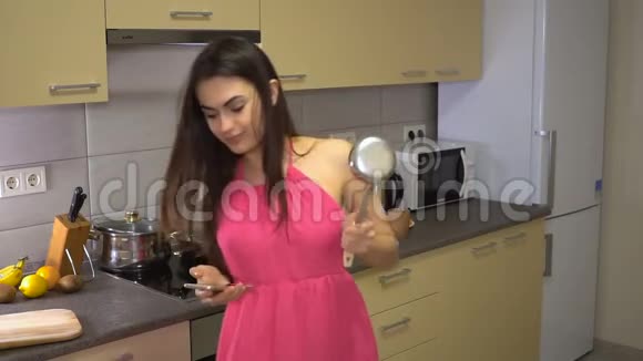 厨房里的女孩用勺子跳舞用电话检查视频的预览图