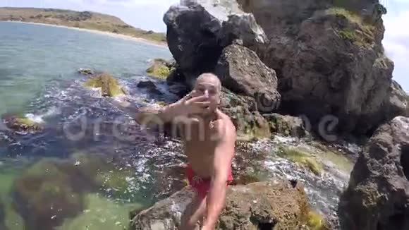 年轻人跳进水里向照相机挥手拇指向上高清慢镜头视频的预览图