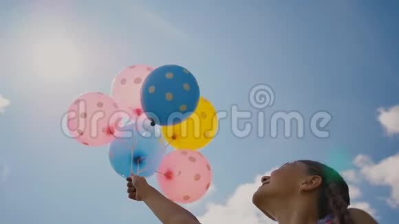 年轻女孩带着鲜艳的彩色球微笑着在相机上摆姿势情绪良好积极向上在夏日的蓝天映衬下视频的预览图