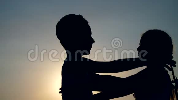 剪影儿童的身影男孩和女孩哥哥和姐姐在夕阳的背景下拥抱视频的预览图