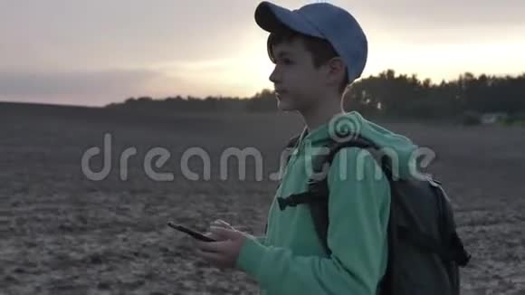 带背包的男孩在日落时散步在户外使用电话旅行概念视频的预览图