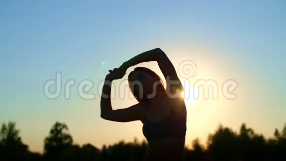 一个长着金色长发的漂亮运动的女孩的轮廓在日落时做运动伸展身体视频的预览图