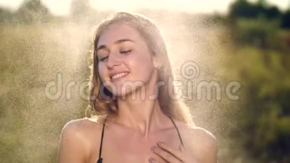 一个性感美丽的年轻金发女孩的肖像在小雨下在阳光下在绿色的草地上女孩视频的预览图