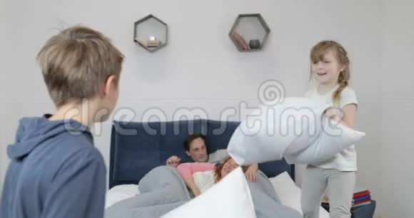 早上幸福的一家人在卧室里两个孩子在枕头上打架幸福的微笑着的父母躺在床上视频的预览图