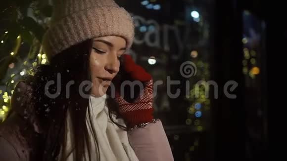 美丽迷人的女孩站在一个装饰着花环的橱窗旁边通过电话交谈新年视频的预览图