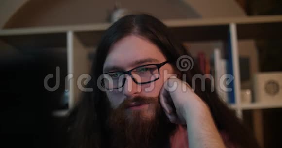 一个留着胡子的年轻人戴着眼镜在黑暗的办公室工作深夜他的脸被屏幕照亮视频的预览图