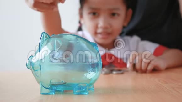 泰国幼儿园的亚洲小女孩穿着校服把钱币放在透明的储蓄罐里选择重点放在省猪钱上视频的预览图
