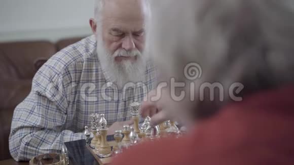 两个正在下棋的成年男子坐在家里的皮革沙发上蓄胡子的人在想哪个棋子能动视频的预览图