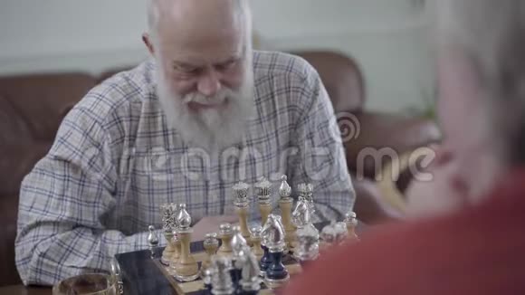 两个老人下棋坐在家里的皮革沙发上蓄胡子的人在想哪个棋子能动视频的预览图