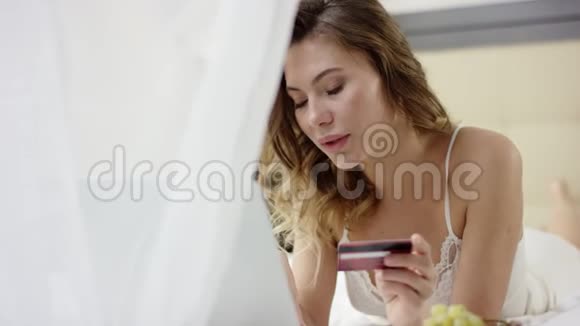 穿着睡衣的漂亮女人躺在床上用笔记本电脑和信用卡视频的预览图