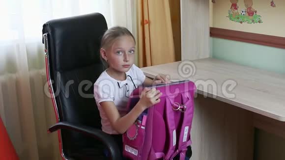 小女孩拿着背包打开它拿出纸笔记本铅笔把笔记本放在桌上坐着的女孩视频的预览图
