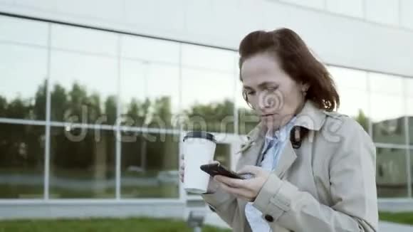 一位年轻漂亮的商业女学生在城市里走来走去喝着咖啡打着电话视频的预览图