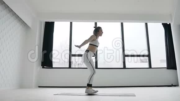 年轻的健身金发女子在健身房附近大窗户锻炼在上午的运动训练锻炼她穿着视频的预览图