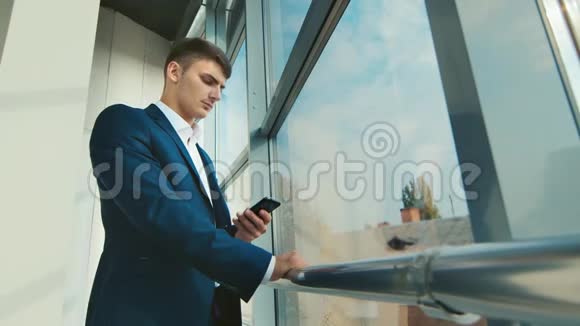 一个穿西装的年轻商人在打电话站在办公室的大窗户旁视频的预览图