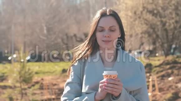 穿外套的年轻黑发女人在城市公园散步喝咖啡的肖像春天视频的预览图