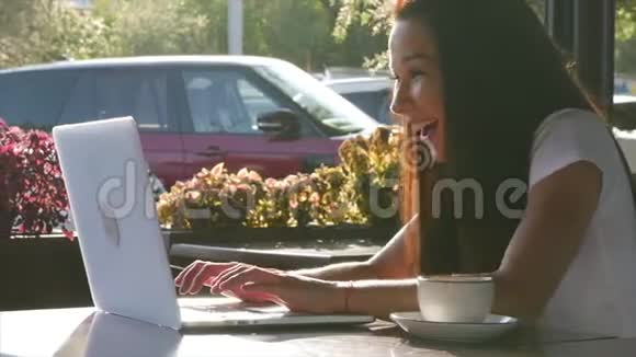 年轻快乐迷人的女人在咖啡馆里喝杯咖啡在笔记本电脑上打字视频的预览图