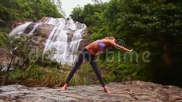 金发女郎在丛林中与美丽的瀑布伸展视频的预览图