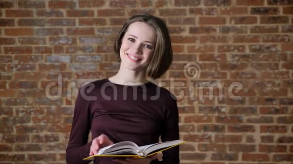 年轻漂亮的女孩正在看书在镜头前看微笑着砖背景视频的预览图