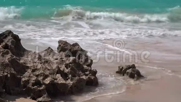 海水泡沫般的海浪冲刷着沙质海岸的珊瑚岩视频的预览图