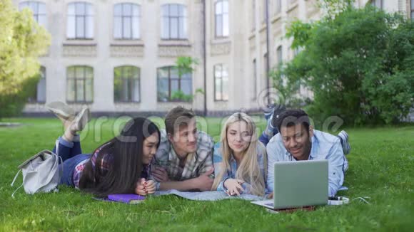 多民族学生躺在草地上在笔记本电脑上看有趣的视频朋友们视频的预览图