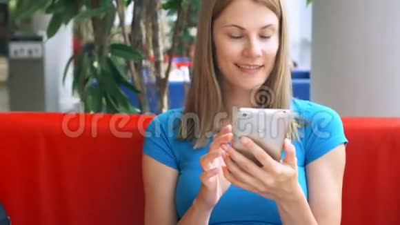 一幅美丽梦幻的年轻女子穿着蓝色t恤坐在咖啡馆里思考的肖像她的智能手机视频的预览图