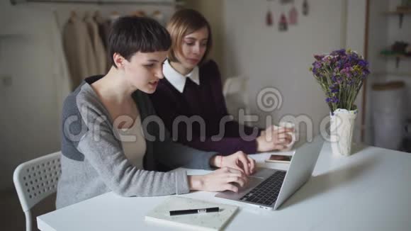 两个女学生坐在桌子上用笔记本上网学习视频的预览图
