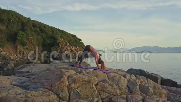 苗条的金发女孩在日出时在岩石上弯曲瑜伽姿势视频的预览图