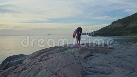 黎明时分空中观景女孩站在石滩上做瑜伽姿势视频的预览图