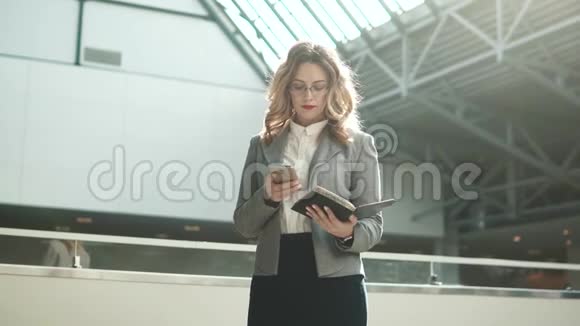 穿着灰色夹克的女商人通过手机发送信息看着智能手表视频的预览图