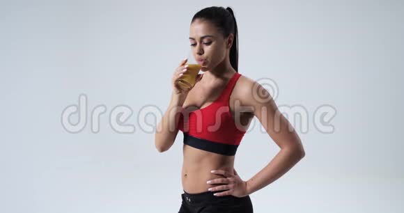 一个漂亮的运动女人喝一杯橙汁在白色背景上隔离慢视频的预览图