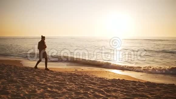 日出时年轻女士沿着冲浪线缓慢地走在海滩上视频的预览图