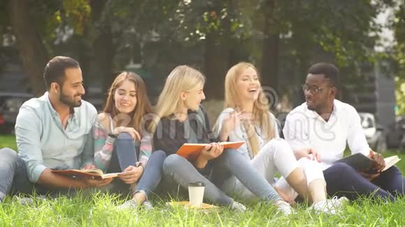 混合种族的学生一起坐在大学校园的绿色草坪上视频的预览图
