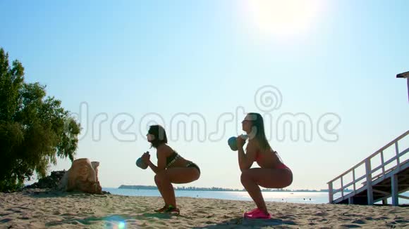 两位运动型年轻女性穿泳衣教练教官表演做举重练习在海滩上视频的预览图