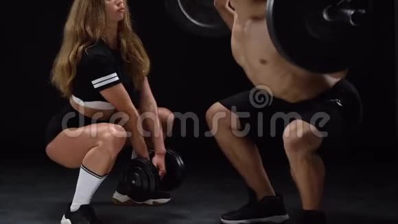 运动的男人和女人蹲在额外的重量训练他们的腿和臀部在一个黑色的背景在工作室视频的预览图