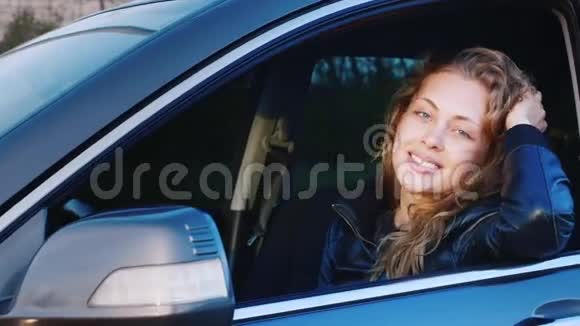 一个年轻的高加索女人在车里的肖像坐在司机座位上看着摄像机微笑着视频的预览图
