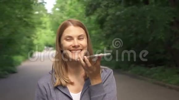 慢动作微笑的女人穿着帽衫在阳光明媚的公园里散步在夏天天打电话视频的预览图