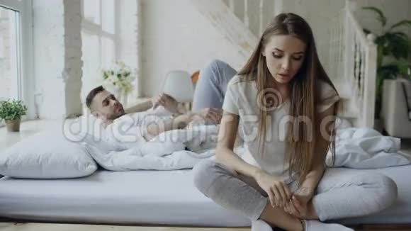沮丧的年轻女子坐在床上哭泣而她的男朋友来拥抱她在家里的卧室里亲吻她视频的预览图