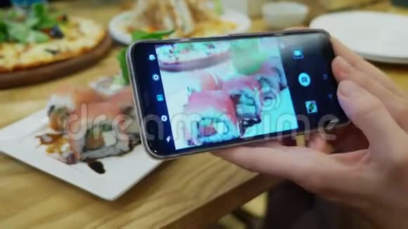 特写镜头女手在餐馆的智能手机上拍寿司视频的预览图