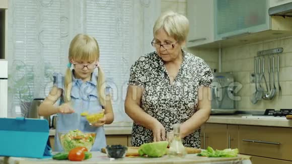 一个6岁的女孩戴着粉红色的眼镜在厨房准备沙拉她奶奶帮忙用平板电脑视频的预览图