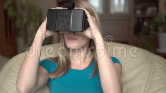 现代休闲女性穿着蓝色t恤坐在家里的椅子上利用她的虚拟现实眼镜视频的预览图