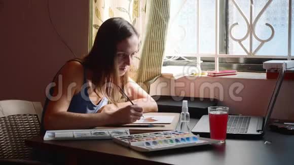 年轻女子在家中通过网上水彩画课视频的预览图